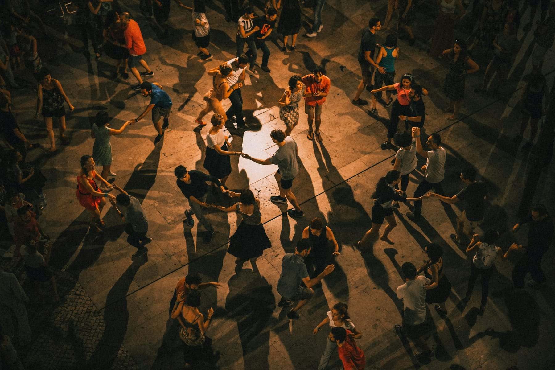Dancers in pairs fill a warm, dimly lit social dance floor, seen from above